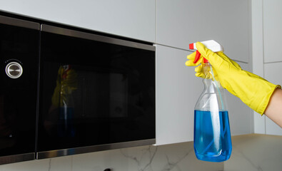 Anti-grease spray in the hand of a girl who is cleaning the kitchen. Cleaning the microwave oven from grease and dirt. Modern antistatic agent. Cleaning company services - 787161231