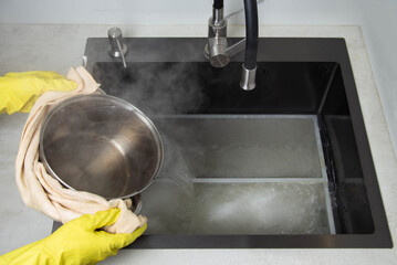 Man's hands in yellow gloves pour pots of hot water into a sink with dirty filters from the hood in the kitchen. Cleaning from dirt and grease with an oxygen cleaner. Copy space for text - 787161240