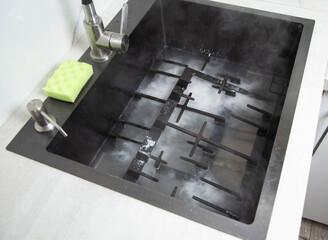 Dirty gas stove grates in the sink with a modern oxygen cleaner for kitchen cleaning. Cleaning the kitchen, removing grease stains, close-up - 787161243