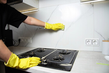 Female hands in yellow gloves with a sponge and detergent wash white porcelain tiles on the wall in the kitchen. Cleaning service. Copy space for text, grease stains - 787161249