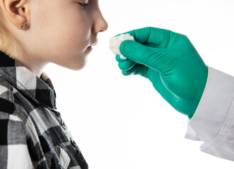 a doctor's hand in a medical glove holds a cotton swab with ammonia to the nose of a seven-year-old girl. White background. Copy space for text. Nasal infection - 787161253