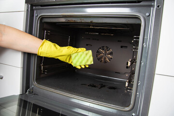 A girl holds a sponge in her hand against the background of an oven. Concept for cleaning electric ovens in the kitchen, cleaning company. Washing up - 787161255