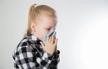 A girl aged seven years old in a checkered shirt blows her nose into a handkerchief on a white background. The concept of nasal congestion due to allergies. Copy space for text - 787161260