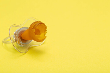 A chewed baby pacifier on a yellow background. Concept of teething in children, close-up. Copy...