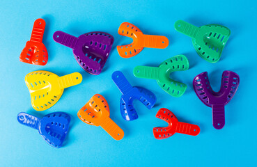 Multi-colored dental spoons for taking an impression of the dental jaw on a blue background. Orthodontics in dentistry. Dental prosthetics and crown manufacturing, close-up