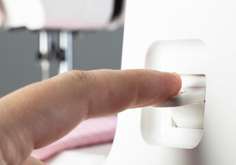 A seamstress's finger switches the reverse key of a sewing machine while sewing, close-up. Industry, regulator