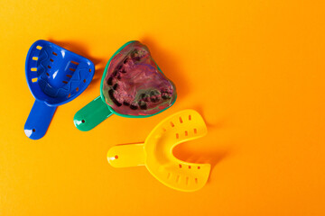 Multi-colored dental spoons for taking an impression of the dental jaw on a orange background. Making an impression of the jaw for braces and dental prosthetics, close-up. Copy space for text