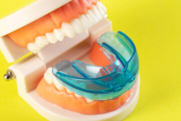 Therapeutic mouthguard on the background of a dental jaw mockup on a yellow background. Treatment of teeth grinding, bruxism in children and adults.  - obrazy, fototapety, plakaty