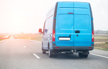 A blue manufactured goods van transports non-food cargo along a highway in the spring against the backdrop of the sun, copy space for text, industry - 787161493