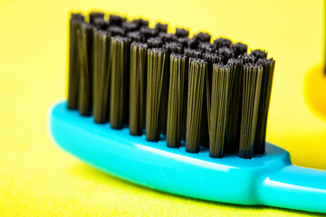 Blue toothbrush with black charcoal coating on a yellow background. Oral care and dental hygiene concept. Prevention of caries, macro, oral cavity