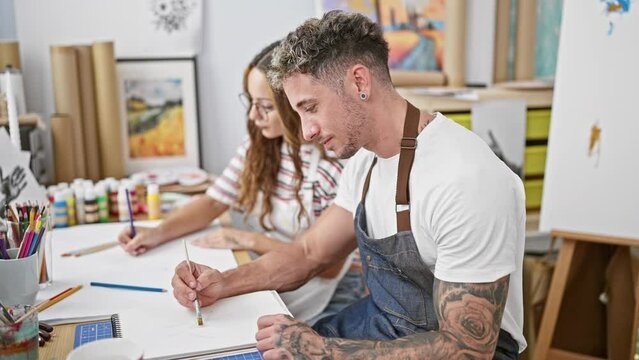 A man and woman focus intently on painting in a well-equipped art studio filled with colorful supplies.