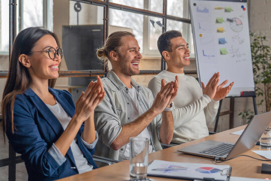 Happy group of businesspeople clapping in office. Young business partners applauding to reporter after listening to presentation at coworking zone