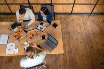 Top view of business people in casual wear sitting at table and having pizza for lunch. Professional colleagues on a break in coworking office, boosting team spirit - obrazy, fototapety, plakaty