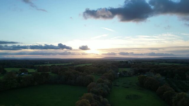 Drone footage of green agricultural field with trees and shrubs at sunset with dark clouds