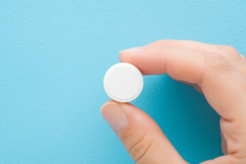 Young adult woman hand fingers holding and showing white pill of c vitamin on light blue table background. Pastel color. Receiving nutrition supplement. Closeup. Top down view. - 787164603