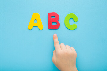 Baby boy hand finger pointing to colorful abc letters on light blue table background. Pastel color. Time to learning. Closeup. Top down view. - 787164657