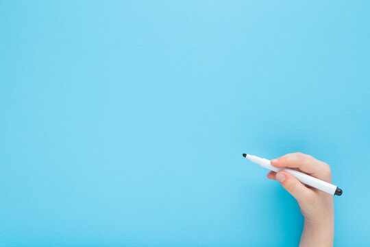 Baby boy hand holding black white color pen and writing on light blue table background. Pastel color. Closeup. Empty place for text. Top down view.