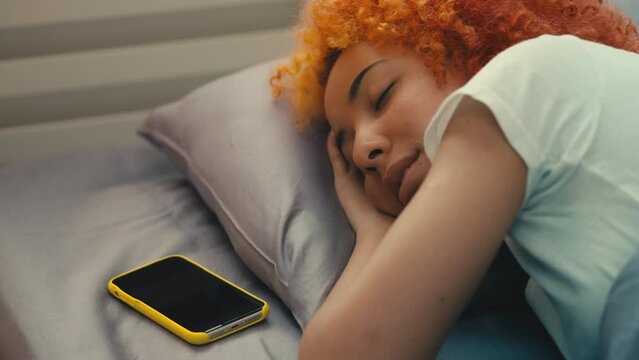 Young African American woman sleeping in the morning, ignoring call from boss