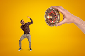 Man in casual clothes protecting himself from hand with a roulette on yellow background
