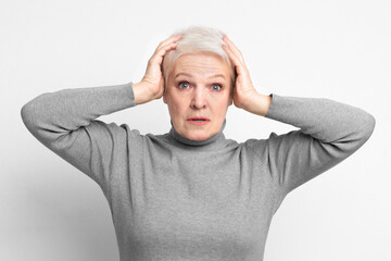 Elderly woman holding head in surprise on grey background