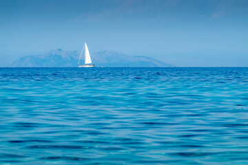 Views of the Mediterranean Sea and a white sailboat on the horizon, on the Greek island of...