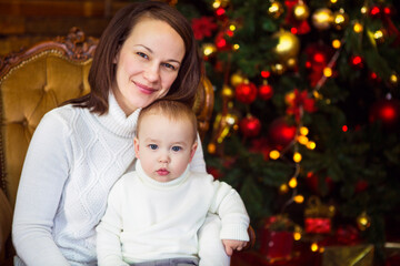Mother with her baby boy siting near the Christmas tree