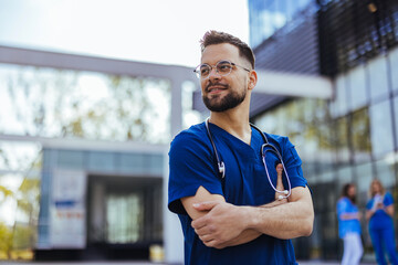 Portrait of smiling male nurse standing in hospital. Portrait Of Male Doctor Wearing Scrubs Standing In Modern Hospital Building. Male healthcare worker smiling outside, portrait - 787171844