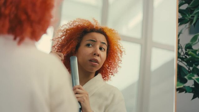 Young woman trying to smooth her frizzy hair with a straightener, beauty device