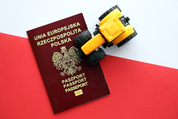 Red polish passport and yellow tractor on smooth red and white flag of Poland close up - obrazy, fototapety, plakaty