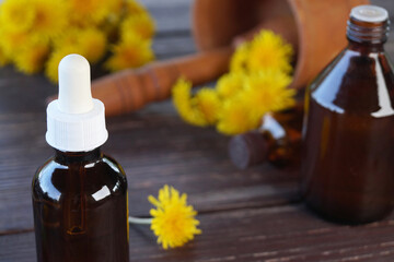Oil in a glass bottle and fresh dandelion flowers on a wooden table. Flower essential oil. Green...