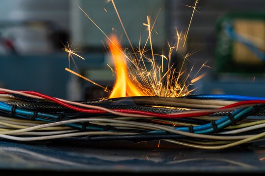 Flames, sparks, smoke between electrical cables, closeup. Short circuit in the twisted wires from the electrical devices, fire hazard concept
