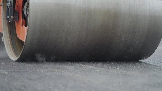 Steamroller compactor cylinder flatten out the new asphalt with steam evaporationg in slow motion. Industrial construction concept