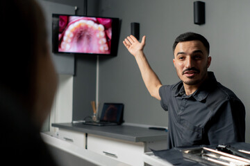 in a dental office man shows a photo of teeth on a monitor for a young beautiful girl consultation