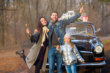 Obraz premium Happy family with Bengal lights by the retro car with presents