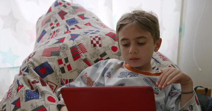 Young boy engrossed in using a digital tablet while relaxing in a cozy bed