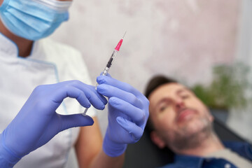 Doctor preparing syringe before beauty procedure on man - 787188075