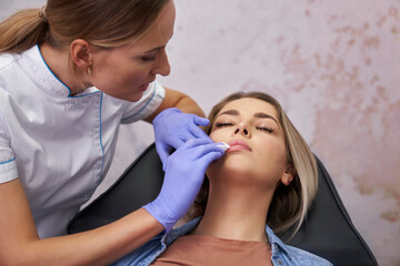 Beautician cleaning patient's face before the beauty procedure