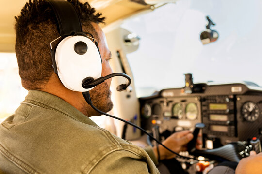 An unrecognizable dark-skinned man is piloting a small plane while wearing headphones. Concept of aircraft rental by the hour. Aviation courses to obtain the aircraft license. Buy an air vehicle.