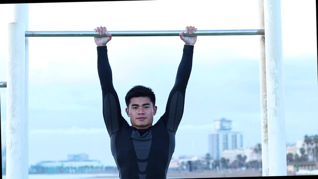 Athletic young man hanging from the bars at the calisthenics gym outdoors