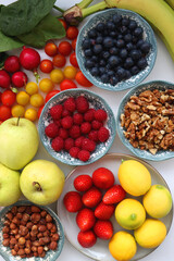 Apples, lemons, bananas, berries, carrots, leek, tomatoes, radishes, spinach and various nuts on white background. Healthy seasonal fruit and vegetable. Top view.