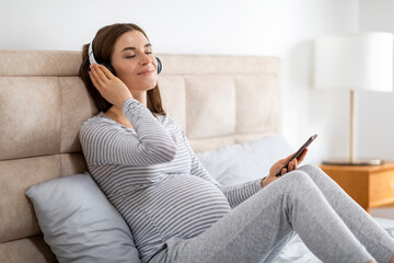 Pregnant woman relaxing with headphones at home
