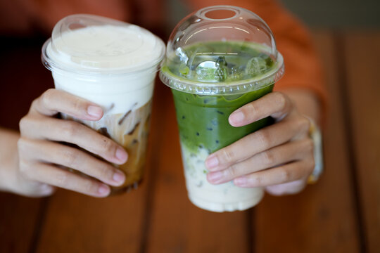 close up and selective focus glass of ice coffee and ice matcha green tea on hands of teenage girls, drinking together at cafe.	