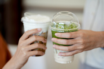 Hands of teenage girls holding glass of ice coffee and ice matcha green tea together at cafe.	