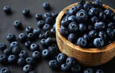 Fresh blueberries in a wooden bowl next to scattered blueberries on a dark background
