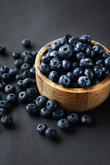 Fresh blueberries in a wooden bowl next to scattered blueberries on a dark background
