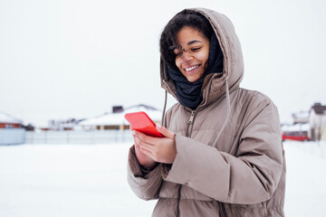 Young charming african woman in warm casual clothes holding red phone in her hands.