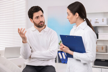 Doctor with clipboard consulting patient during appointment in clinic