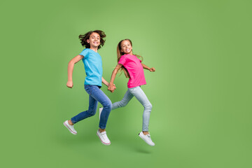 Fototapeta na wymiar Full length photo of cheerful cute friends wear t-shirts jumping high walking arms empty space isolated green color background