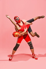 Athlete in red costume with mask executing wrestling move against partner dressed same costume against pink studio background. Concept of pop art, difference, costume festivals, competitions. Ad