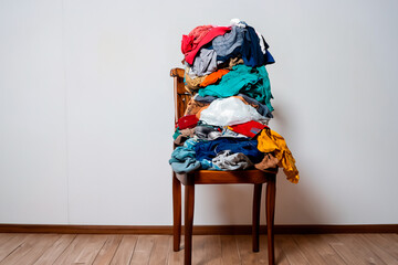 A pile of clothes stacked on a chair near the wall. The concept of overconsumption
